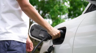 İlerici adam elektrikli aracına elektrik kablosu takıyor. Ev şarj istasyonundan EV arabası. Çevreyi korumak için temiz ve yenilenebilir enerji kullanan elektrikli bir araba. Çevre dostu otomobil.