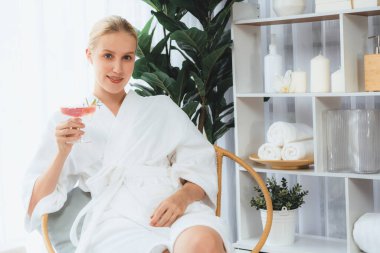 Güzellik ya da vücut bakımı güzellik salonu yaşam tarzı konsepti. Bornoz giyen bir kadın lüks otel kaplıcalarında ya da tatil odasında içkiyle rahatlıyor. Tatil ve boş zaman rahatlığı. Sessiz.