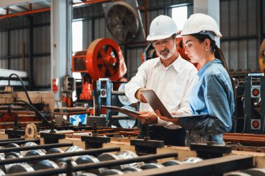 Metal imalatında makine mühendisliği denetleyicisi olarak liderlik örneğini sunan çelik endüstriyel makineyi incelemek için dizüstü bilgisayar kullanan fabrika mühendisi ve asistan..