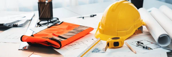 Architectural designed building blueprint layout and engineer tool for designing blueprint with contractor project document on engineer workspace table in office with safety helmet or hardhat. Insight