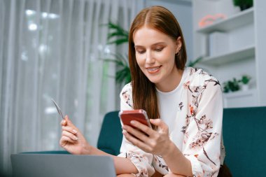 Genç mutlu kadın internetten alışveriş yaparak ürün satın alırken aynı zamanda internet üzerinden online ödeme sistemi ile çevrimiçi mağaza platformundan en yüksek siber güvenlik tarafından korunan ürünler sipariş ediyor.