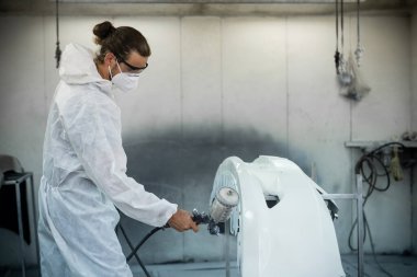 Koruyucu ekipmanlı otomotiv işçisi araba kaportasına sprey tabanca ya da oda atölyesindeki solunum boyasıyla renk boyası uyguluyor. Tamir için araba boyama servisi. Oxus.