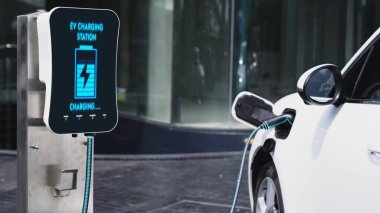 Şehir merkezinin otoparkındaki şarj istasyonuna bağlı elektrikli araba. Alternatif temiz ve sürdürülebilir enerji kullanan geleceğin yenilikçi yenilenebilir EV arabası. İnceleyin