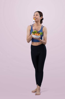 Spor giyim mağazasında elinde meyve ve sebze dolu salata kasesi tutan genç bir Asyalı kadın. Doğal gençlik ve uygun vücut yaşam tarzı izole edilmiş arka planda dengeli beslenme. Kuvvetli