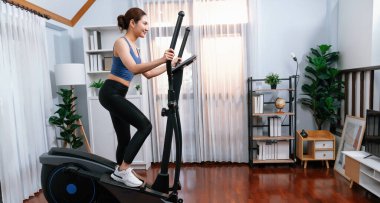 Enerjik ve güçlü atletik Asyalı kadın evde eliptik koşu makinesiyle koşuyor. Formda fiziğin takibi ve ev çalışması ve eğitimle sağlıklı yaşam tarzına bağlılık. Kuvvetli