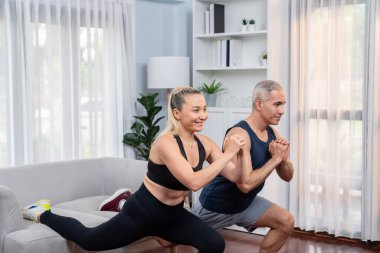 Aktif ve formda yaşlı çiftler oturma odasında egzersiz yapmadan önce mobilya kullanarak ısınma ve esneme hareketleri yapıyorlar. Emeklilikten sonra sağlıklı yaşam tarzı konsepti. Etki