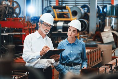 Metal imalatında makine mühendisliği denetleyicisi olarak liderlik örneğini sunan çelik endüstriyel makineyi incelemek için dizüstü bilgisayar kullanan fabrika mühendisi ve asistan..