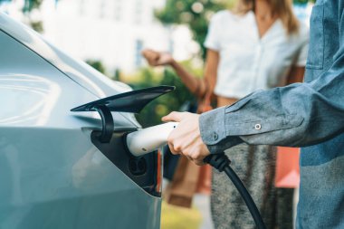 Genç çift yazın yeşil sürdürülebilir şehir bahçesinde EV elektrikli araba ile seyahat ederken, yeşil temiz yeniden şarj edilebilir elektrikli araç iç organları ile kentsel sürdürülebilirlik yaşam tarzını gösteriyor.