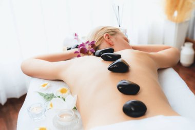 Lüks tatil köyündeki kaplıcalarda sıcak taş masajı. Gün ışığı sükunet ortamında, mutlu kadın müşteri bazalt taş masajından zevk alıyor. Rahatlatıcı bir sıcaklıkla vücudun üzerinde süzülüyor. Sessiz.