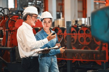 Metal imalatında makine mühendisliği denetleyicisi olarak liderlik örneğini sunan çelik endüstriyel makineyi incelemek için dizüstü bilgisayar kullanan fabrika mühendisi ve asistan..