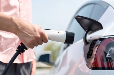 Dışarıdaki şarj istasyonundan EV şarj aletini şarj etmek için elektrikli araca elle tak. Alternatif temiz ve sürdürülebilir enerji kavramına sahip taze gün ışığı ortamı. Kalıcı