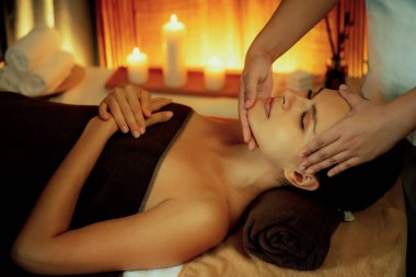 Beyaz kadın stres önleyici kafa masajı yapmaktan ve lüks otel veya otelde sıcak mum ışığında yüz güzelliği eğlencesi yapmaktan zevk alıyor. Sessiz.