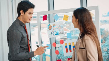 İş adamları ofisteki proje planlama kurulunda çalışıyor ve proje gelişimini analiz etmek için iş arkadaşlarıyla sohbet ediyorlar. Düzenli olması için cama yapıştırılmış yapışkan notlar kullanıyorlar. Jivy