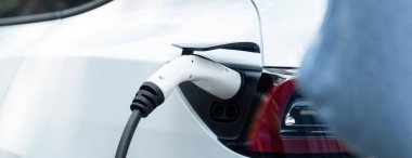 Panorama kapatma EV şarj kolu fişe takıldı veya elektrikli arabaya bağlandı, temiz çevre için sıfır CO2 emisyonu ile alternatif ve sürdürülebilir enerjiyle EV araba aküsünü şarj etti. Kalıcı
