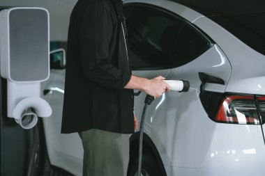 Genç adam EV elektrikli arabasıyla alışveriş merkezinin otoparkına gidiyor şehir merkezindeki şarj oluyor yeşil, temiz, yeniden şarj edilebilir elektrikli araç iç organları ile kentsel sürdürülebilirlik yaşam tarzını gösteriyor