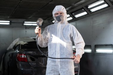 Tam korumalı ekipmanlı otomotiv işçisi sprey tabanca ya da oda atölyesindeki solunum cihazı boyasıyla araba kaportasına ustalıkla renk boyası uygular. Tamir için araba boyama servisi. Oxus.