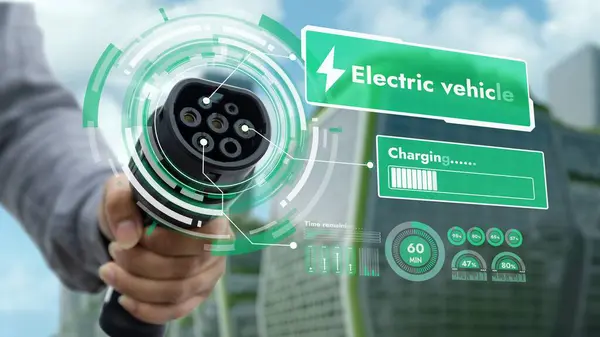 Focus EV charger pointing in front of camera display smart digital battery status hologram with businessman hand in blur ESG green cityscape background. Electric car charger using clean energy. Peruse