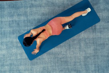Spor giyimli Asyalı kadın spor kıyafetleri içinde spor paspası üzerinde spor eğitimi rutini olarak burpee yapıyor. Çekici kız sağlıklı yaşam tarzını ve formda vücut yapısını takip eder. Kuvvetli