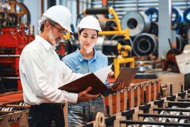 Metal imalatında makine mühendisliği denetleyicisi olarak liderlik örneğini sunan çelik endüstriyel makineyi incelemek için dizüstü bilgisayar kullanan fabrika mühendisi ve asistan..