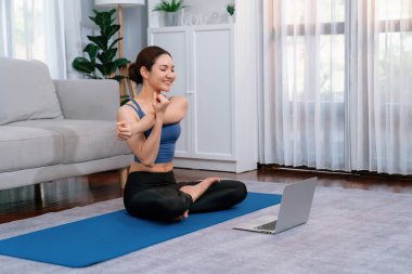 Spor kıyafetli Asyalı bir kadın spor salonunda antrenman yaparken spor minderinde yoga yapıyor. Sağlıklı vücut bakımı kadın dizüstü bilgisayardan yoga videosu izliyor. Kuvvetli