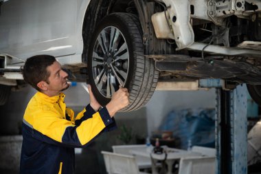 Araba kaldırma istasyonunun altında çok çalışan bir tamirci araba tekerleğini değiştiriyor. Otomotiv işçisi lastik lastiği değiştiriyor. Profesyonel araba bakımı ve bakımı konseptinde. Oxus.