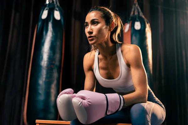 アジアの女性ムエタイのボクサーやキックボクシングは 背景にボクシング機器とジムで彼女の手袋で座って短い休憩を取る 力強く筋肉質なボディスポーツ女性 インペトゥス — ストック写真