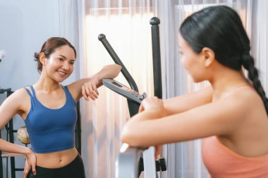 Enerjik ve güçlü atletik Asyalı kadın evde spor arkadaşı ya da antrenörü ile birlikte eliptik koşu makinesiyle koşuyor. Formda fiziğin takibi ve sağlıklı yaşam tarzına bağlılık. Kuvvetli