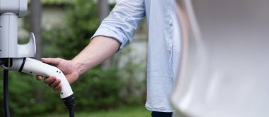 Çevre dostu bilinçli adam EV şarj istasyonundan modern elektrikli aracı şarj ediyor. EV araba teknolojisi gelecekteki sürdürülebilirlik için alternatif ulaşım aracı olarak kullanılıyor. Panorama Eşzamanlaması