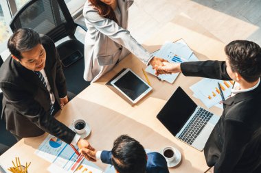 Grup iş adamları toplantı masasında el sıkışırken üst açıdan kendilerine güvenirler. Genç işadamı ve işkadını işçiler yatırım anlaşması imzaladılar. Jivy