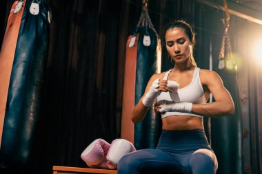 Kararlı Asyalı kadın Muay Thai boksörü kaslı, fiziksel olarak hazır ya da boks eldiveni giymiş, ya da boks eldiveni giymiş, spor salonundaki ringde yoğun boks antrenmanına hazırlanıyor. Impetus