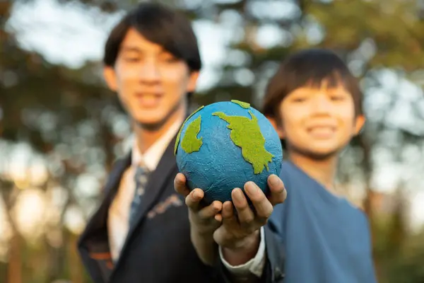 Focus Earth with blurred asian boy and businessman holding globe together as Earth day concept as corporate social responsible to make greener environmental for sustainable future generation. Gyre