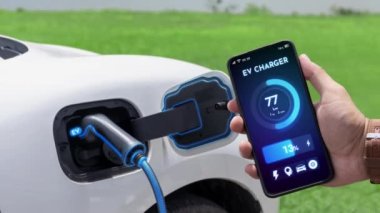 Akıllı telefon ekran akü durumu arayüzünü elinde tutan iş adamı akıllı EV mobil uygulama ile EV otomobili elektrik şarj istasyonundan doğal göl arka planı ile elektrik. İnceleyin.