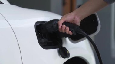 Adam garajdaki şarj istasyonundan elektrikli arabasını EV şarj cihazıyla şarj ediyor. EV arabaların teknolojik gelişimi ve gelecekteki sürdürülebilir enerji için ev enerjisi altyapısı. İnceleyin