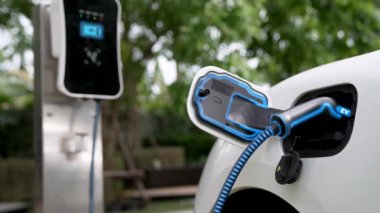Doğal yeşil araba parkındaki ekolojik temiz enerji şarj istasyonundan gelen fütürist akıllı EV şarj aletinin şarj ettiği elektrikli araba. Alternatif enerji kullanan gelecekçi çevre dostu elektrikli araba. İnceleyin
