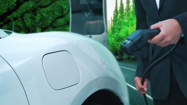 進歩的なビジネスマンは 緑の森の近くの充電ポイントから彼の電気自動車を充電するのを停止します 将来の環境を守るために持続可能でクリーンなエネルギーによって駆動されるEv車 — ストック動画