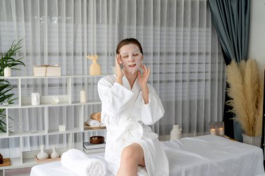 Kaplıca salonunun sakin, modern gün ışığı atmosferi, kadın müşteri poz veriyor ve yüz maskesi ile gençleştiriyor. Yüz bakımı ve güzellik kozmetolojisi prosedürü. Sessiz.