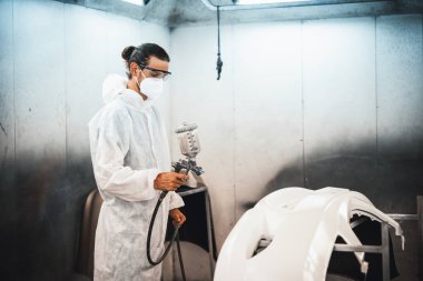Koruyucu ekipmanlı otomotiv işçisi araba kaportasına sprey tabanca ya da oda atölyesindeki solunum boyasıyla renk boyası uyguluyor. Tamir için araba boyama servisi. Oxus.