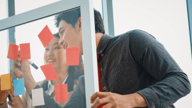 İş adamları ofisteki proje planlama kurulunda çalışıyor ve proje gelişimini analiz etmek için iş arkadaşlarıyla sohbet ediyorlar. Düzenli olması için cama yapıştırılmış yapışkan notlar kullanıyorlar. Jivy