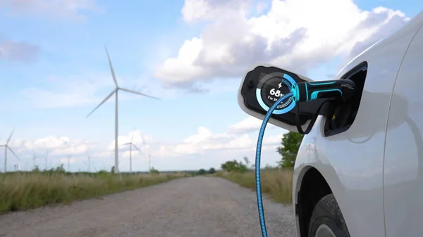 Electric car recharging energy from EV charging station display futuristic smart battery status hologram by EV charger plug cable in wind turbine farm. Alternative clean energy sustainability. Peruse