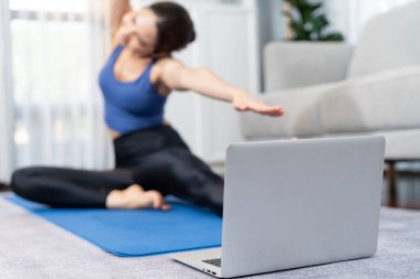 Çevrimiçi egzersiz videolarını gösteren yere odaklanmış dizüstü bilgisayar. Sportif atletik kadın ise arka planda ısınma ve esneme hareketleri üzerine yoğunlaşıyor. Kuvvetli