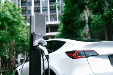Yazın yeşil sürdürülebilir şehir bahçesinde elektrikli araba şarj oluyor. Kentsel sürdürülebilirlik yaşam tarzı yeşil temiz yeniden şarj edilebilir enerji elektrikli BEV araç iç organları
