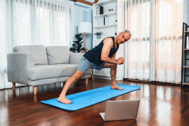 Aktif ve formda bir adam, evde egzersiz yapmadan önce ısınma ve esneme hareketleri yapıyor ve çevrimiçi fitness videosu izliyor. Emekliler için sağlıklı yaşam tarzı konsepti. Etki