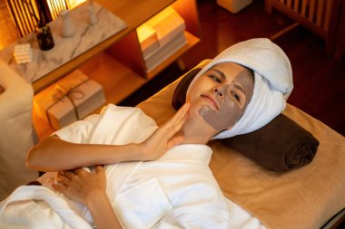 Kaplıca salonunun sakin atmosferi, üst düzey kadın müşteri sıcak mum ışığında kömür kömürü yüz kremi masajıyla kendini yenilemeye çalışıyor. Yüz bakımı ve güzellik konsepti. Sessiz.