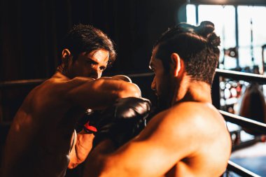 Asyalı ve Kafkasyalı Muay Thai boksörü boks maçında dirsek atağı yapıyor. Güçlü kaslı bir boksör acımasız bir dövüş hüneriyle yumruk ve dirsek yumruğa dövüşüyor. Impetus