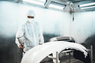 Tam korumalı ekipmanlı otomotiv işçisi sprey tabanca ya da oda atölyesindeki solunum cihazı boyasıyla araba kaportasına ustalıkla renk boyası uygular. Tamir için araba boyama servisi. Oxus.