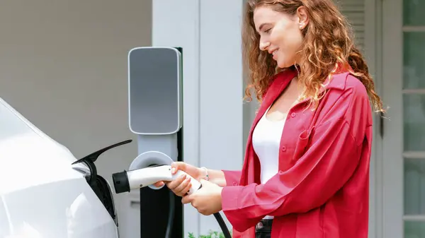 现代环保妇女从家用电动汽车充电站为电动汽车充电 电动汽车技术应用于居家居民的未来环境的可持续性 同步操作 — 图库照片