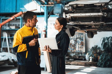 İki araç tamircisi birlikte çalışıyor, dizüstü bilgisayarla araba teftişi yapıyor. Üniformalı otomotiv servis teknisyeni hatayı tanımlamak için dikkatle sorun çıkartıyor. oxus