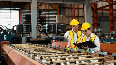 Ağır sanayi fabrikasındaki çelik üretim hattında endüstriyel malların optimal kalitede üretimi için mühendis tarafından denetlenirken fabrika işçisi metal damgalama makinesini çalıştırıyor. Örnek gösteriliyor