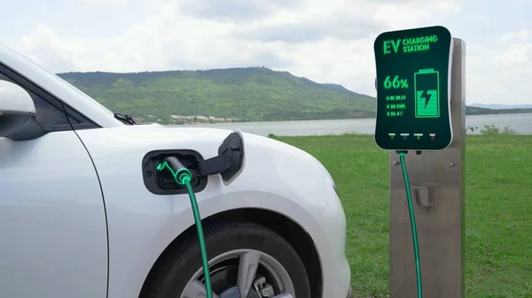 充電ステーションに接続された電気自動車は 自然と湖の背景とEv充電ケーブルでバッテリーを充電します 将来の革新的なEv車とエネルギー持続可能性 Peruse — ストック写真