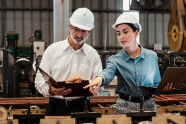 Metal imalatında makine mühendisliği denetleyicisi olarak liderlik örneğini sunan çelik endüstriyel makineyi incelemek için dizüstü bilgisayar kullanan fabrika mühendisi ve asistan..